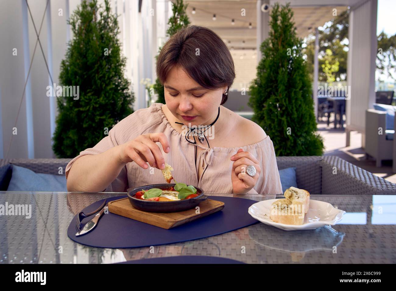 Una donna di medie dimensioni in un abito da pesca che mangia Shakshouka in un ristorante moderno Foto Stock