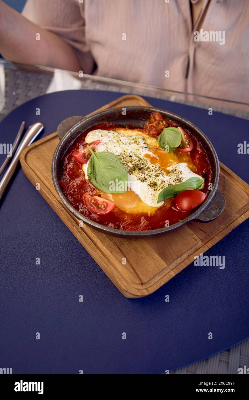 Una donna di medie dimensioni in un abito da pesca che mangia Shakshouka in un ristorante moderno Foto Stock