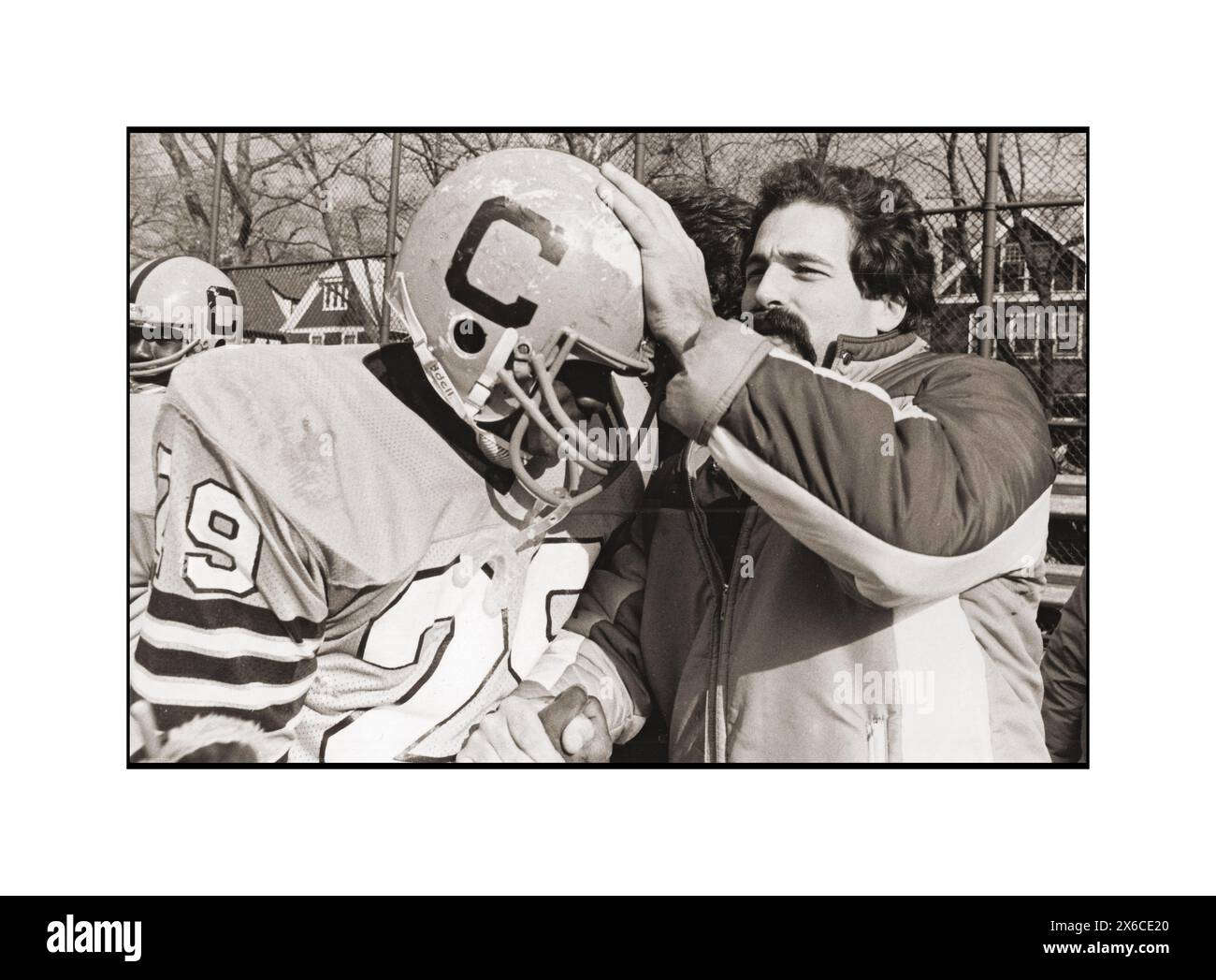 Un allenatore della squadra di calcio delle scuole superiori di Canarsie si congratula con un giocatore dopo una vittoria scuotendo la mano e stringendo il casco. Al Midwood Field di Brooklyn nel 1982. Foto Stock