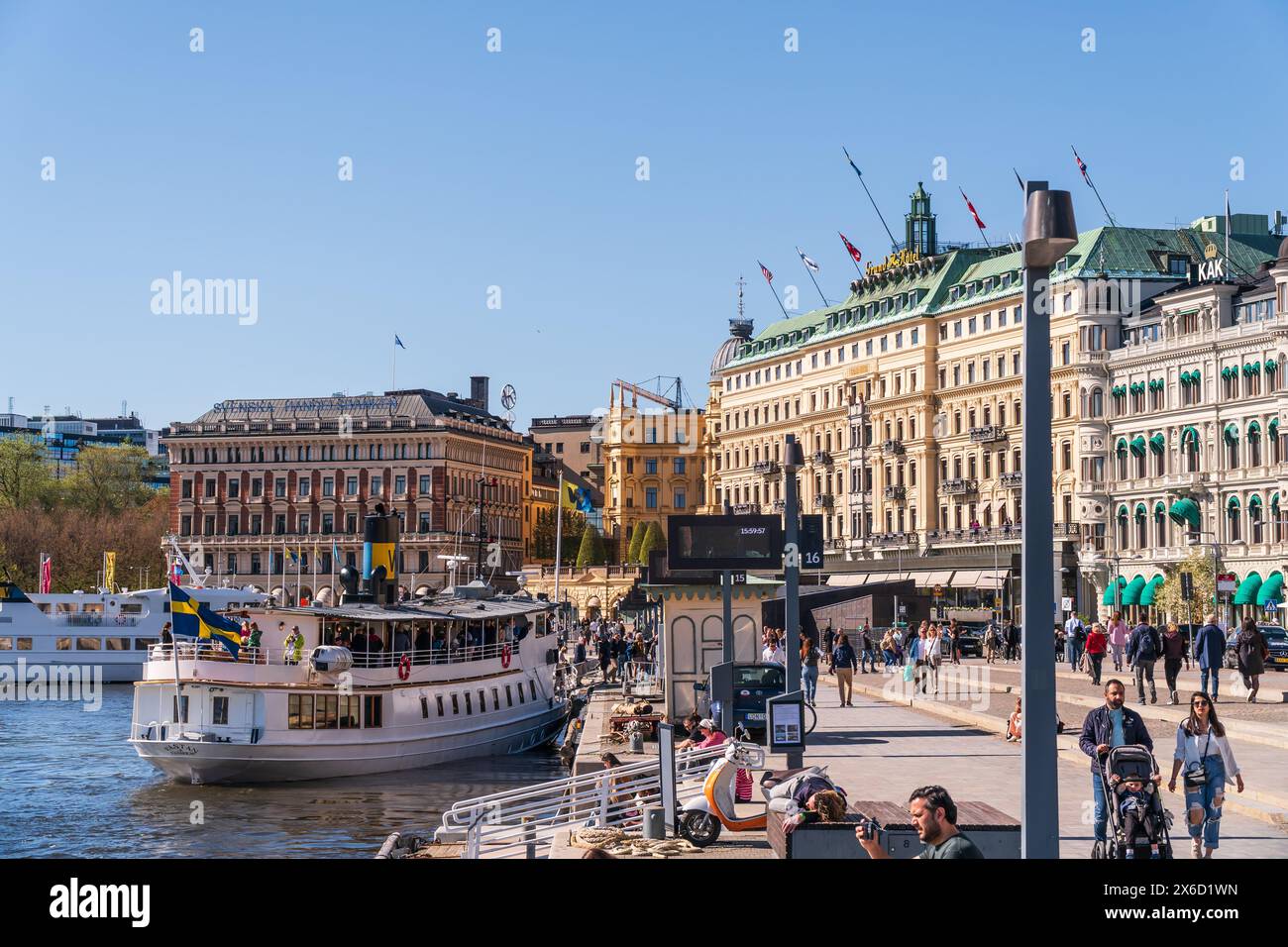 Il Grand Hotel e le persone che camminano lungo le vie d'acqua vicino a Strömkajen, un luogo popolare per le barche turistiche e i battelli pendolari. Primavera e sole luminoso Foto Stock