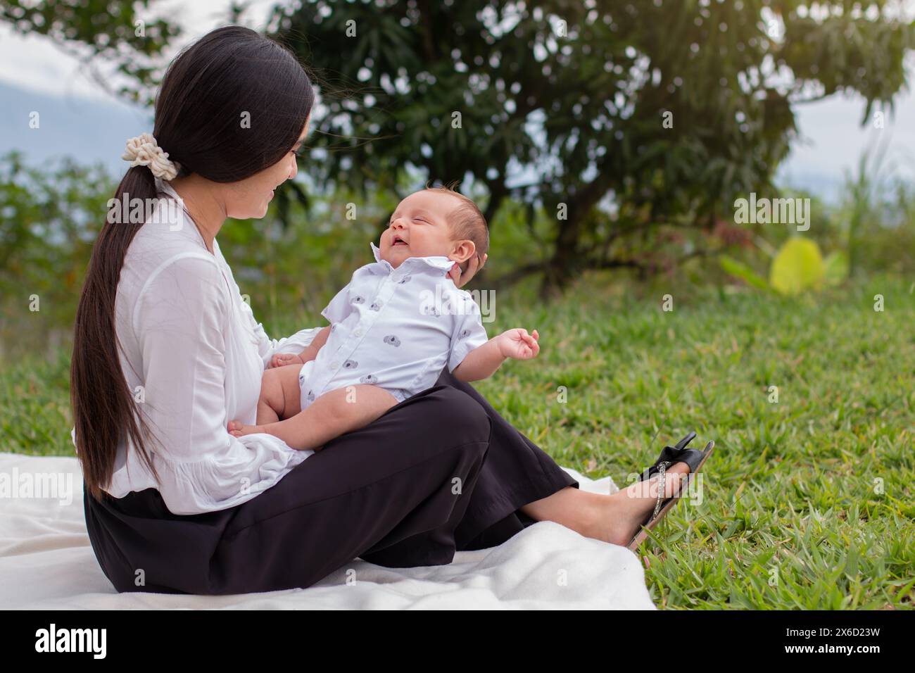 stile di vita: una madre seduta nel prato che tiene il bambino e sorride felicemente Foto Stock