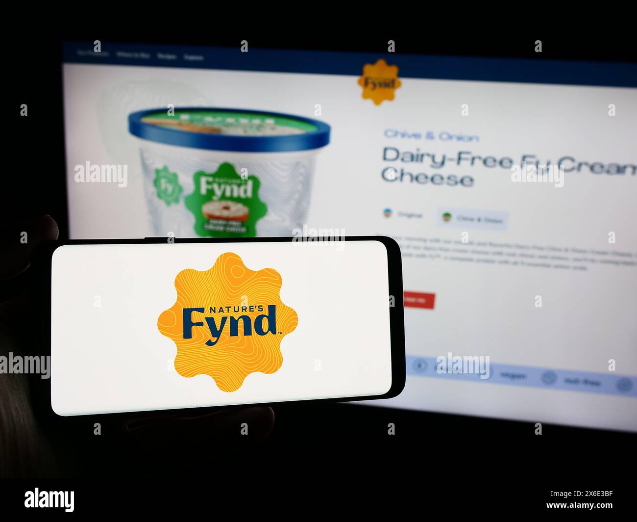 Persona che possiede uno smartphone con il logo della società statunitense The Fyn­der Group Inc. (Nature's Fynd) davanti al sito Web. Mettere a fuoco il display del telefono. Foto Stock