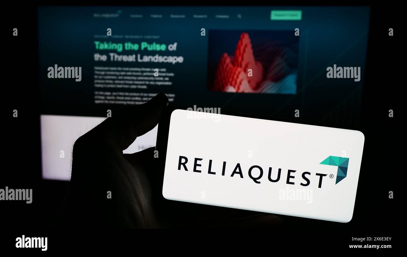 Persona che possiede uno smartphone con il logo della società statunitense di sicurezza informatica ReliaQuest LLC davanti al sito Web. Mettere a fuoco il display del telefono. Foto Stock