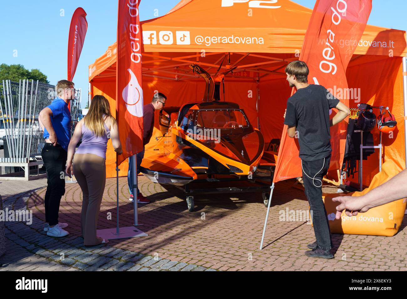 Klaipeda, Lituania - 11 agosto 2023: Un gruppo di individui si riunisce intorno a una tenda arancione in un campo. Foto Stock