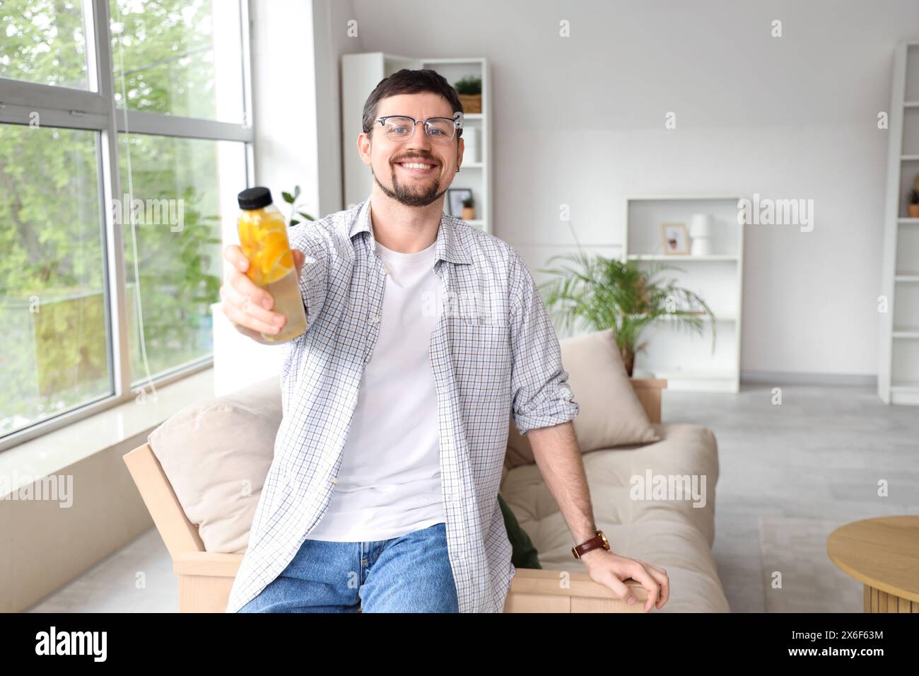 Giovane con una bottiglia di acqua di limone a casa Foto Stock