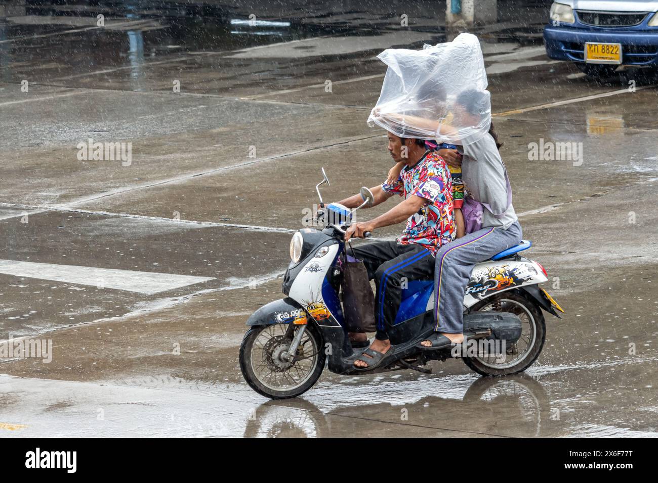SAMUT PRAKAN, THAILANDIA, 20 Mar 2024, Una famiglia guida una moto sotto la pioggia e si protegge con una grande borsa di plastica Foto Stock