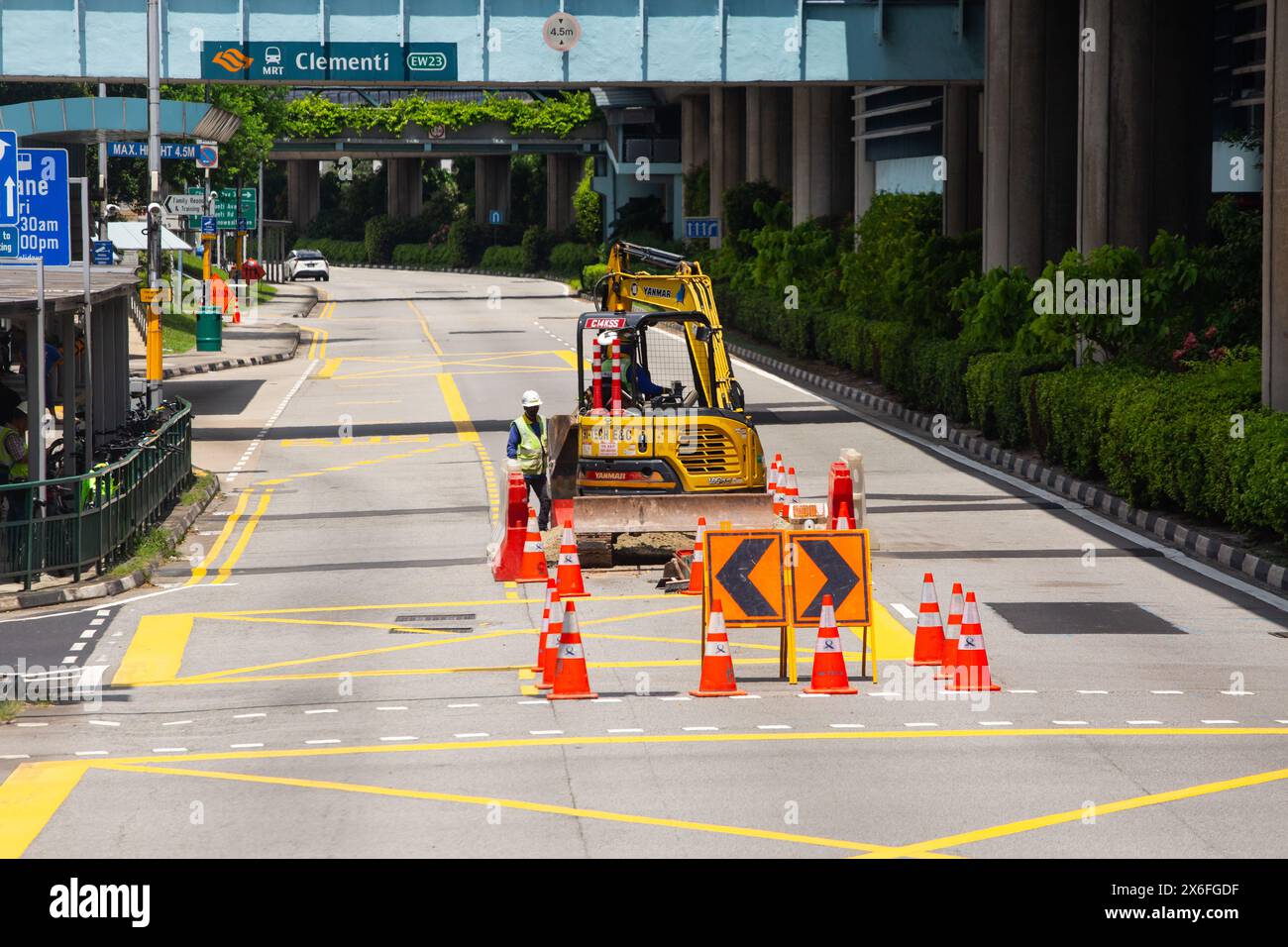 Miniescavatori che eseguono lavori stradali in mezzo alla strada. I segnali di avvertimento sono disposti per deviare i veicoli in arrivo a sinistra e a destra. Singapore. Foto Stock