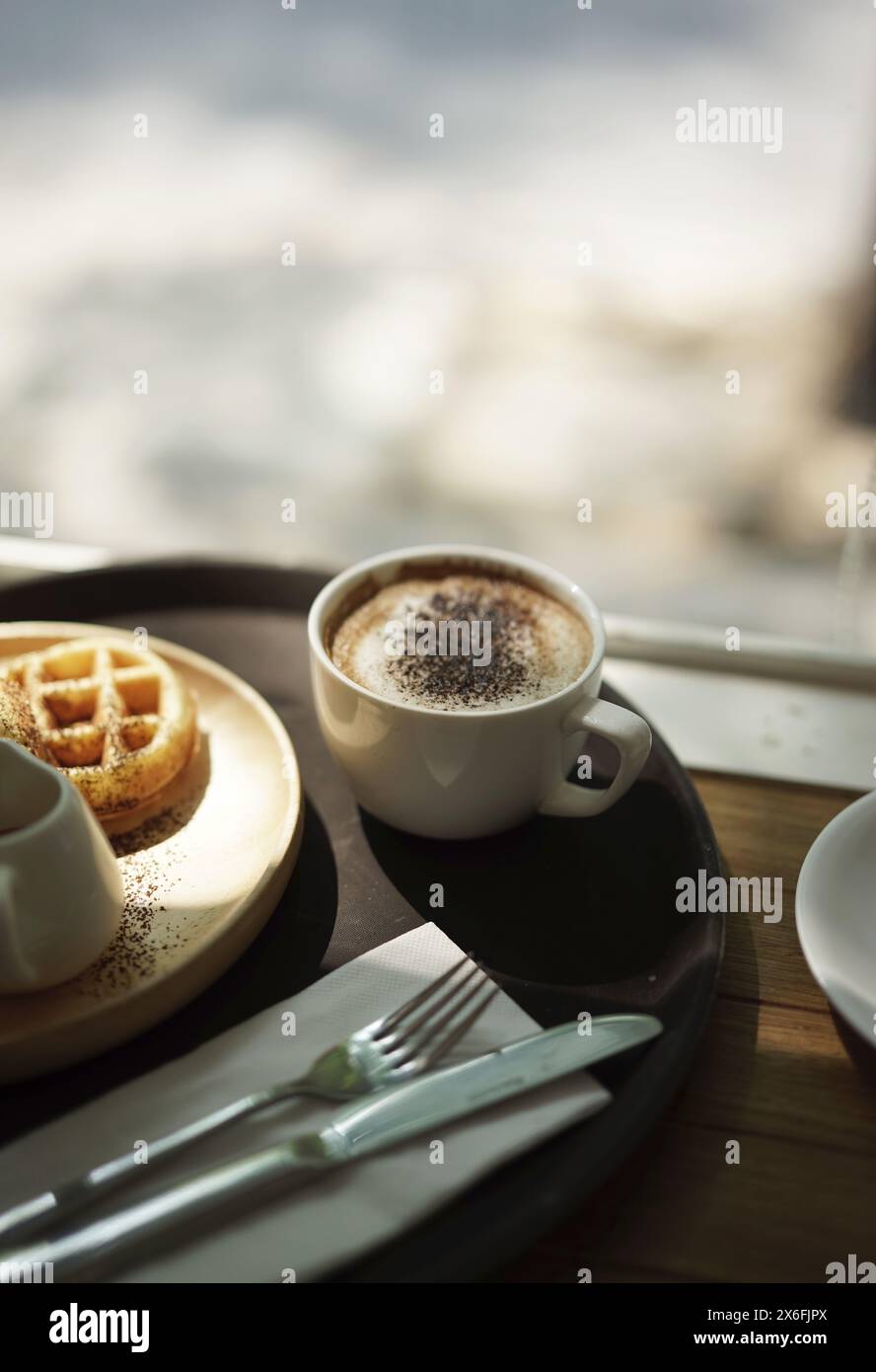Caffè cappuccino e waffle con forchetta e coltello sullo sfondo bokeh alla luce del sole. Foto Stock