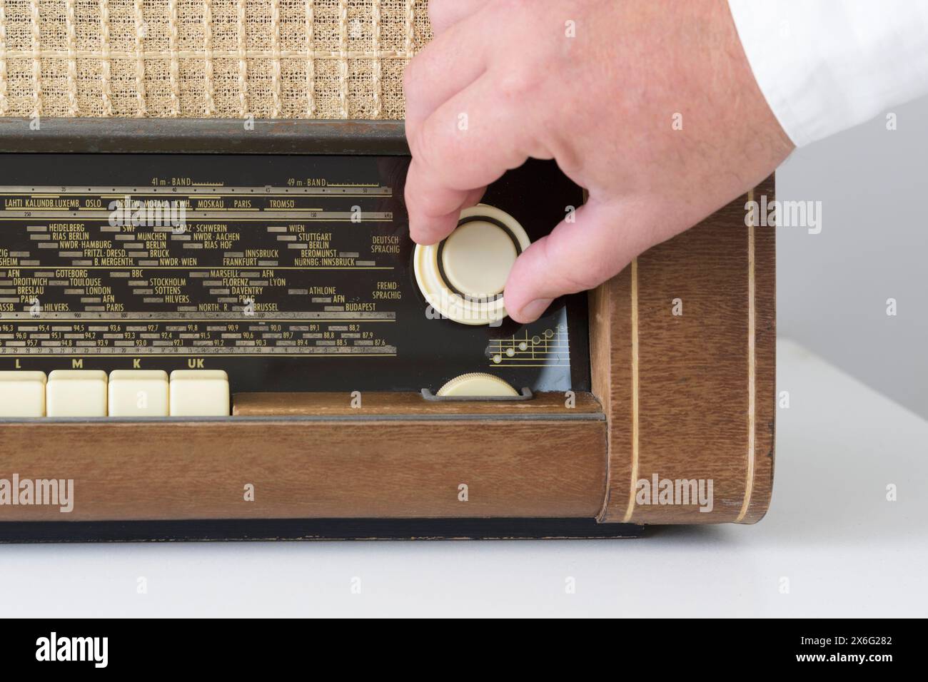 Vera radio dagli anni '50 agli anni '60 Su un tavolo bianco. Tracce di tempo. La mano di un uomo sul quadrante radio imposta l'onda. Primo piano Foto Stock