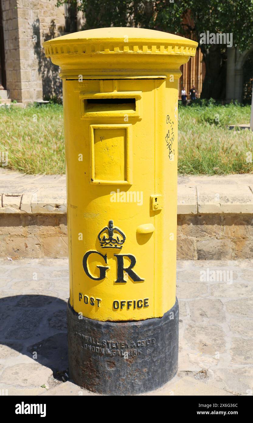 FAMAGOSTA, CIPRO DEL NORD - 08 MAGGIO 2024: Vecchia cassetta postale inglese d'epoca gialla con erba e sfondo a muro Foto Stock