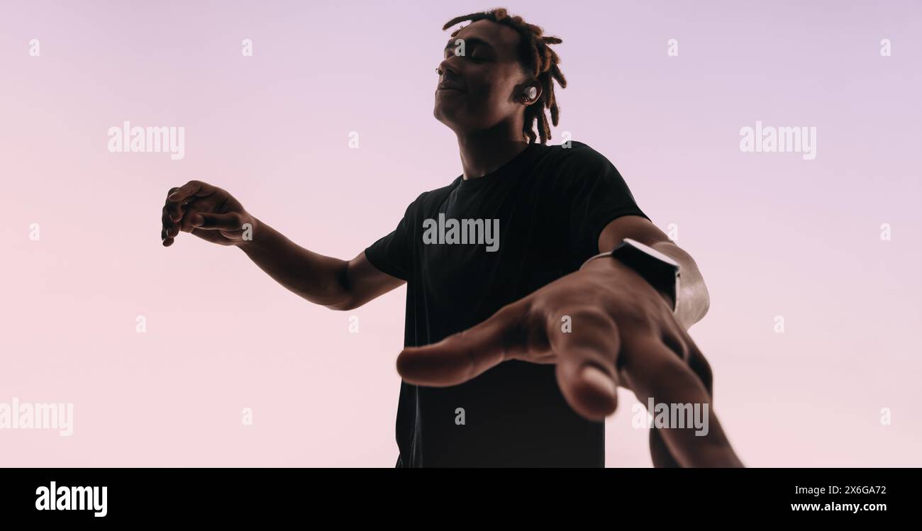 Un giovane con i dreadlock danzerà energicamente al ritmo di una canzone sullo sfondo di uno studio. Gli occhi chiusi e le mani aggraziate mostrano la sua passione Foto Stock