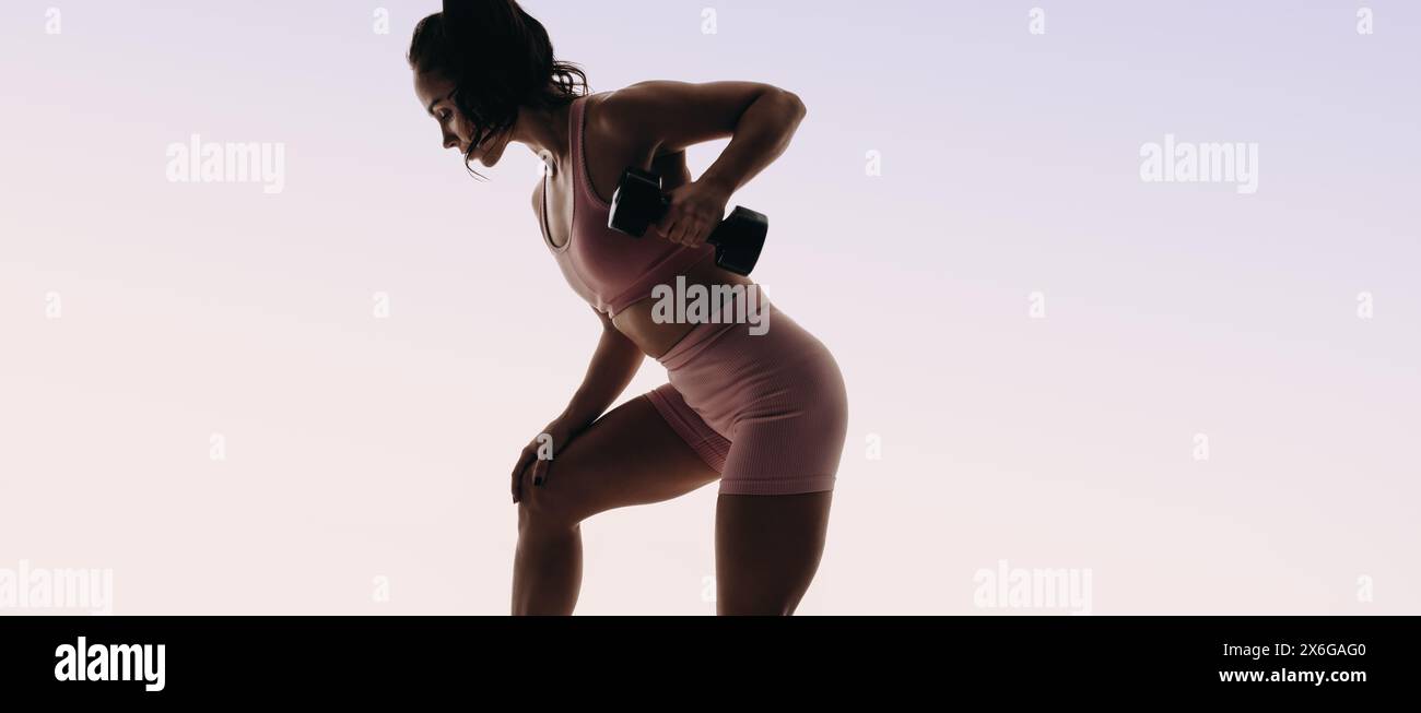 Indossa un'atleta femminile in abbigliamento sportivo che esegue una routine di sollevamento pesi in uno studio. Trasuda forza mentre solleva un manubrio e si mette in macchina Foto Stock