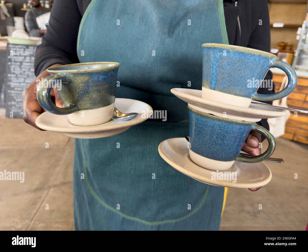 Cape Occidentale, Sudafrica. 20. 04. 2024. Cameriera che pulisce il tavolo e tiene tre tazze e piattini. Foto Stock