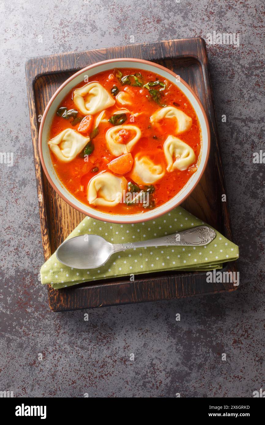Zuppa vegetariana di tortellini di pomodoro con verdure e spinaci primo piano in un piatto sul tavolo. Vista dall'alto verticale Foto Stock