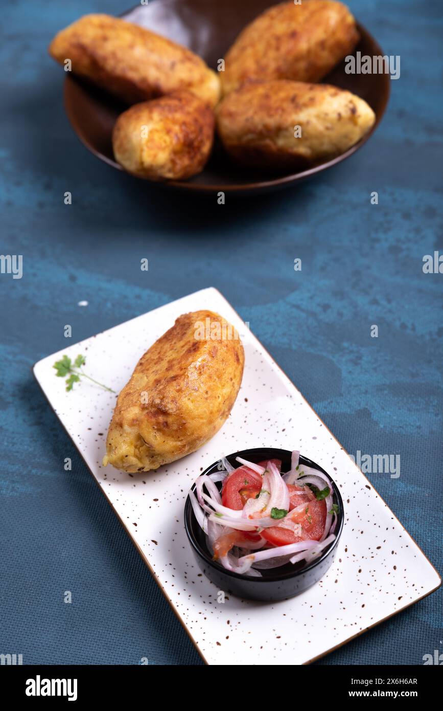 Vista dall'alto di una patata croccante con ripieno salato all'interno, accompagnata da una cipolla e insalata di pomodoro. Foto Stock