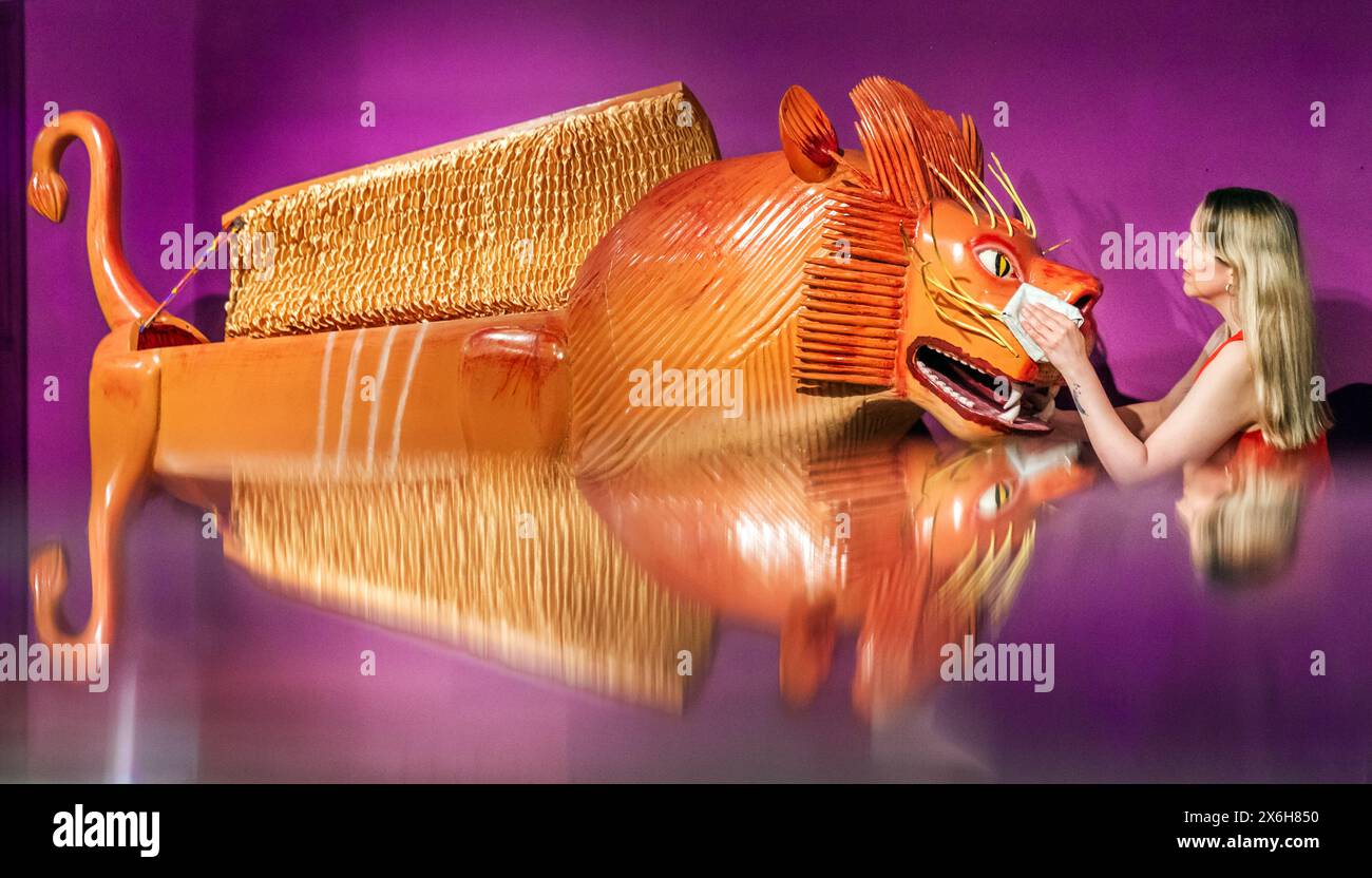 Kat Baxter curatore di archeologia, pulisce una bara a forma di leone (riflessa in un armadietto di vetro) realizzata dal famoso falegname ghanese Paa Joe, noto per la scultura di abebuu adekai, o "proverbi box", che mirano a catturare elementi della vita della persona defunta. La bara fa parte della mostra Living with Death al Leeds City Museum, che esplora i diversi modi in cui le persone sperimentano la morte, la morte e il dolore. Data foto: Mercoledì 15 maggio 2024. Foto Stock