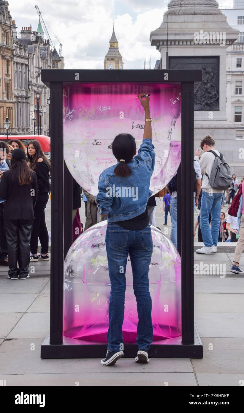 Londra, Inghilterra, Regno Unito. 15 maggio 2024. Una donna firma una grande clessidra a Trafalgar Square, parte di una campagna di Female Invest che mira a colmare il divario finanziario di genere. Secondo l'organizzazione, ci vorranno attualmente 169 anni per colmare il divario e stanno incoraggiando le donne ad entrare in borsa per accelerare il cambiamento. (Credit Image: © Vuk Valcic/ZUMA Press Wire) SOLO PER USO EDITORIALE! Non per USO commerciale! Foto Stock