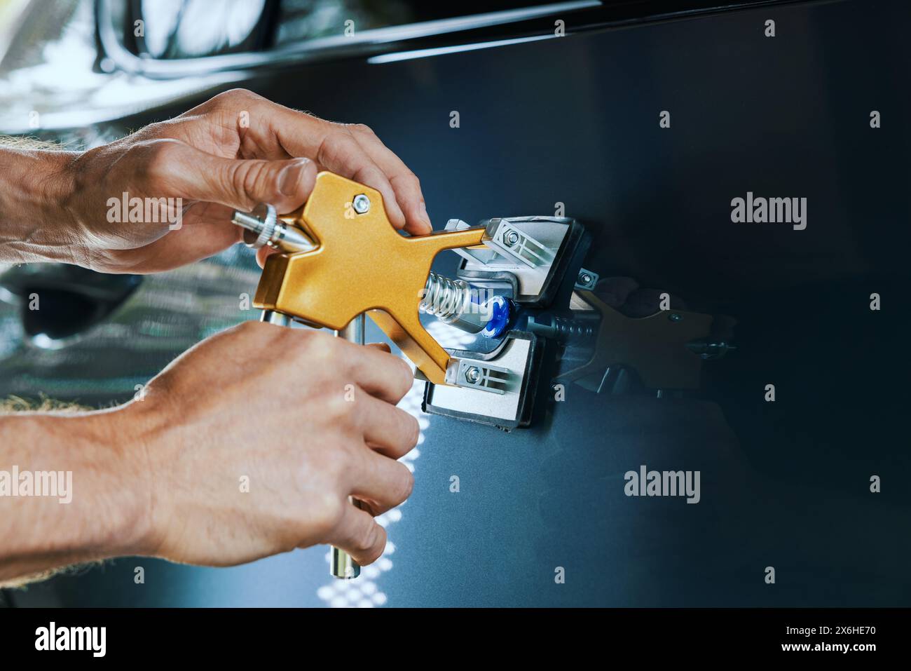 attrezzo di riparazione ammaccature per auto senza verniciatura. Uomo che fissa la portiera del veicolo con tecnologia PDR Foto Stock