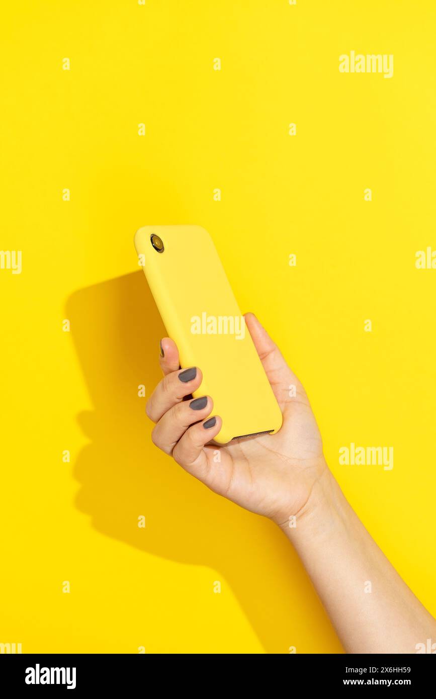 Tenere a mano il telefono con copertina gialla su sfondo giallo Foto Stock