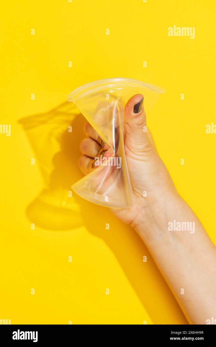 Tenere a mano il bicchiere di plastica monouso su sfondo giallo Foto Stock