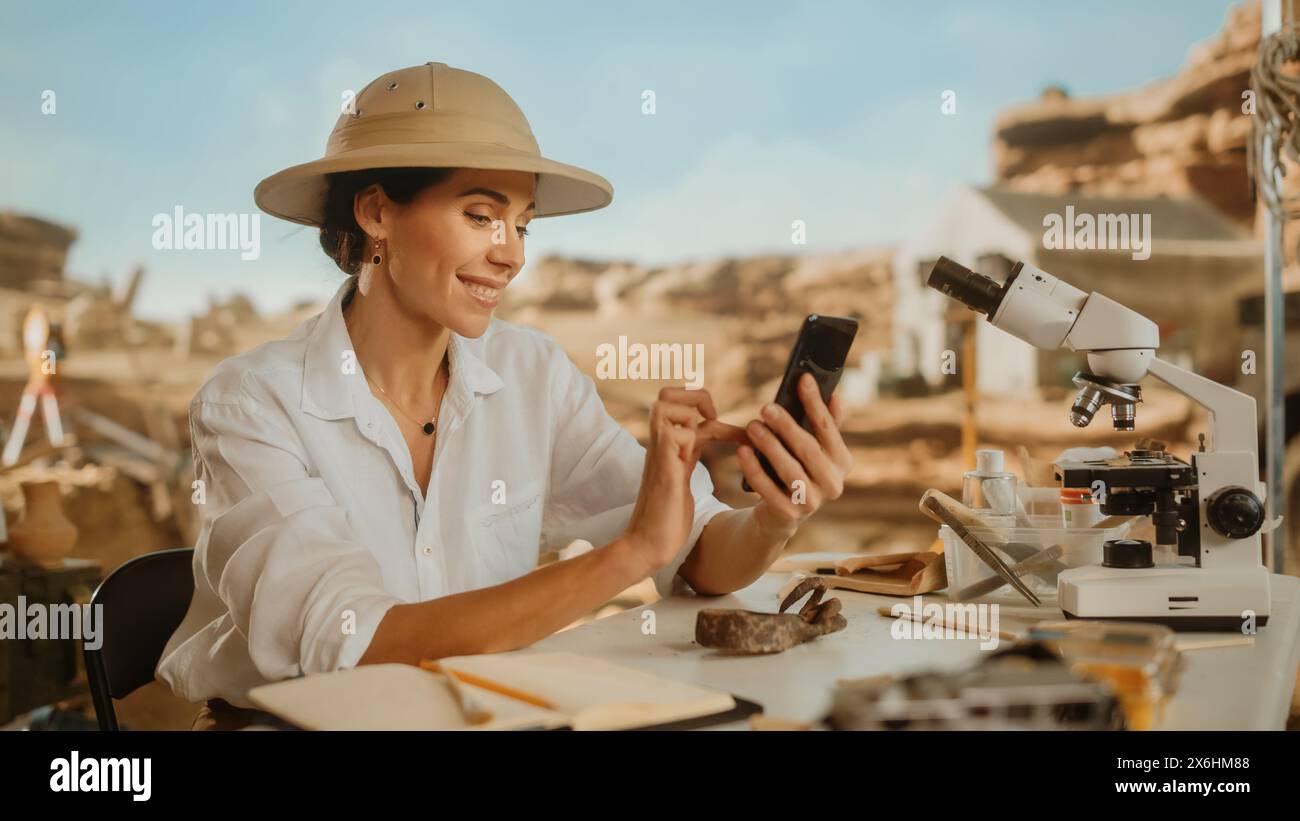 Sito di scavo archeologico: Famosa archeologa femminile che fa ricerca, utilizza lo smartphone per pubblicare la scoperta dei resti fossili, manufatti della cultura della civiltà antica sui social media di Internet Foto Stock