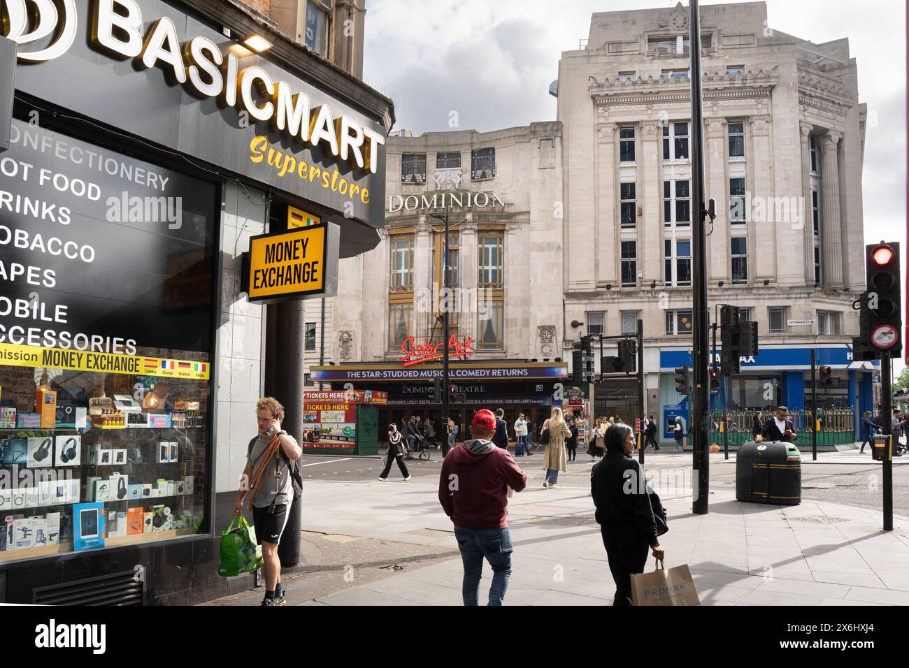 I pedoni attraversano Tottenham Court Road, Londra, vicino al Dominion Theatre, mentre sono visibili un superstore BasicMart e un cambio valuta. Foto Stock