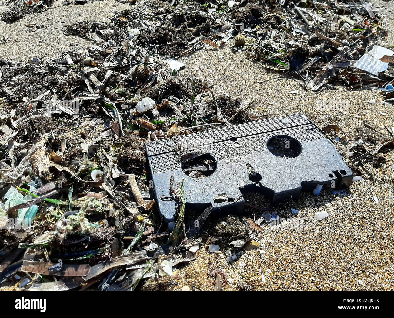 Nastro VHS scartato su una spiaggia stracciata, riflettendo l'impatto duraturo dei rifiuti di plastica. Questa immagine cattura una fetta del passato impigliata in quella di oggi Foto Stock