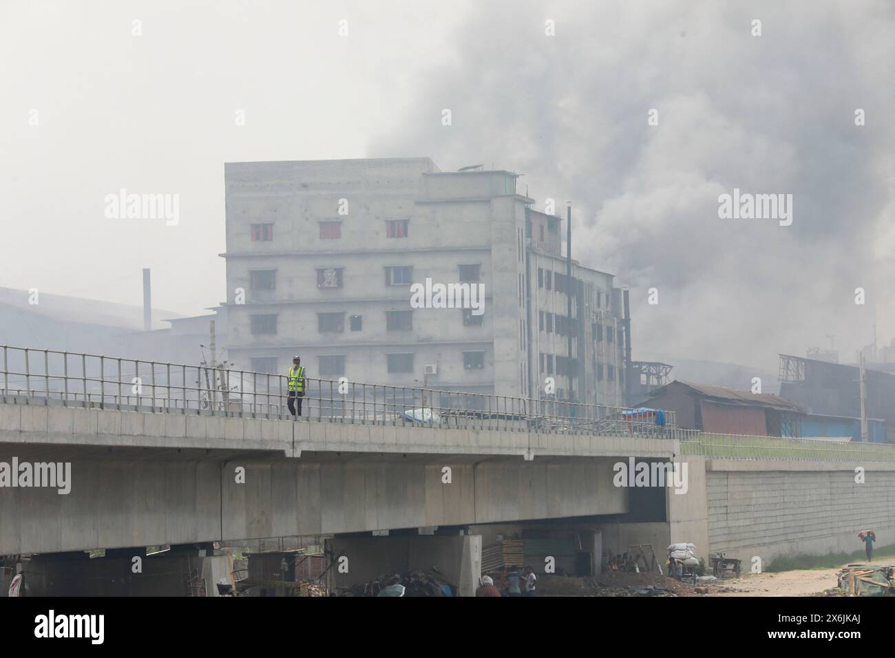 Dacca, Bangladesh. 15 maggio 2024. La gente passa un'area industriale mentre il fumo sale dai mulini rilaminati a Shyampur, a Dacca, Bangladesh, 15 maggio 2024. Secondo uno studio della Banca mondiale, il Bangladesh deve affrontare un elevato livello di inquinamento atmosferico, che costa circa il 9% del PIL all'anno. La maggior parte dei laminatoi in acciaio all'interno e intorno alla capitale sono stati eseguiti senza il necessario sistema di controllo dell'inquinamento atmosferico che poneva un rischio di inquinamento atmosferico e di pericolo per la salute. Foto di Suvra Kanti Das/ABACAPRESS. COM credito: Abaca Press/Alamy Live News Foto Stock
