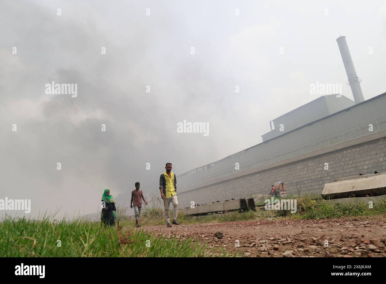 Dacca, Bangladesh. 15 maggio 2024. La gente passa un'area industriale mentre il fumo sale dai mulini rilaminati a Shyampur, a Dacca, Bangladesh, 15 maggio 2024. Secondo uno studio della Banca mondiale, il Bangladesh deve affrontare un elevato livello di inquinamento atmosferico, che costa circa il 9% del PIL all'anno. La maggior parte dei laminatoi in acciaio all'interno e intorno alla capitale sono stati eseguiti senza il necessario sistema di controllo dell'inquinamento atmosferico che poneva un rischio di inquinamento atmosferico e di pericolo per la salute. Foto di Suvra Kanti Das/ABACAPRESS. COM credito: Abaca Press/Alamy Live News Foto Stock