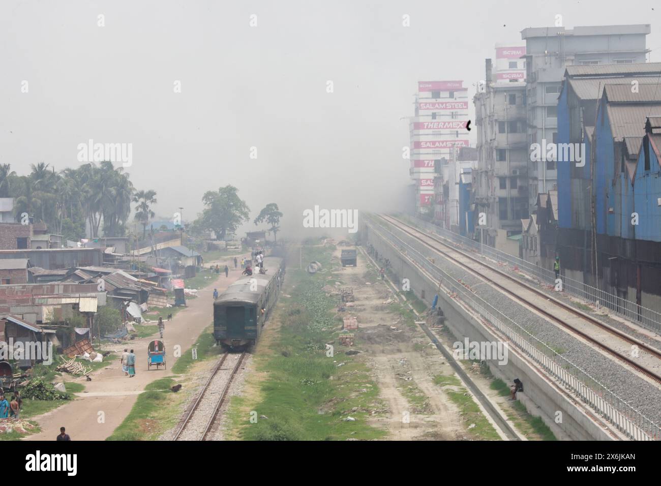 Dacca, Bangladesh. 15 maggio 2024. La gente passa un'area industriale mentre il fumo sale dai mulini rilaminati a Shyampur, a Dacca, Bangladesh, 15 maggio 2024. Secondo uno studio della Banca mondiale, il Bangladesh deve affrontare un elevato livello di inquinamento atmosferico, che costa circa il 9% del PIL all'anno. La maggior parte dei laminatoi in acciaio all'interno e intorno alla capitale sono stati eseguiti senza il necessario sistema di controllo dell'inquinamento atmosferico che poneva un rischio di inquinamento atmosferico e di pericolo per la salute. Foto di Suvra Kanti Das/ABACAPRESS. COM credito: Abaca Press/Alamy Live News Foto Stock