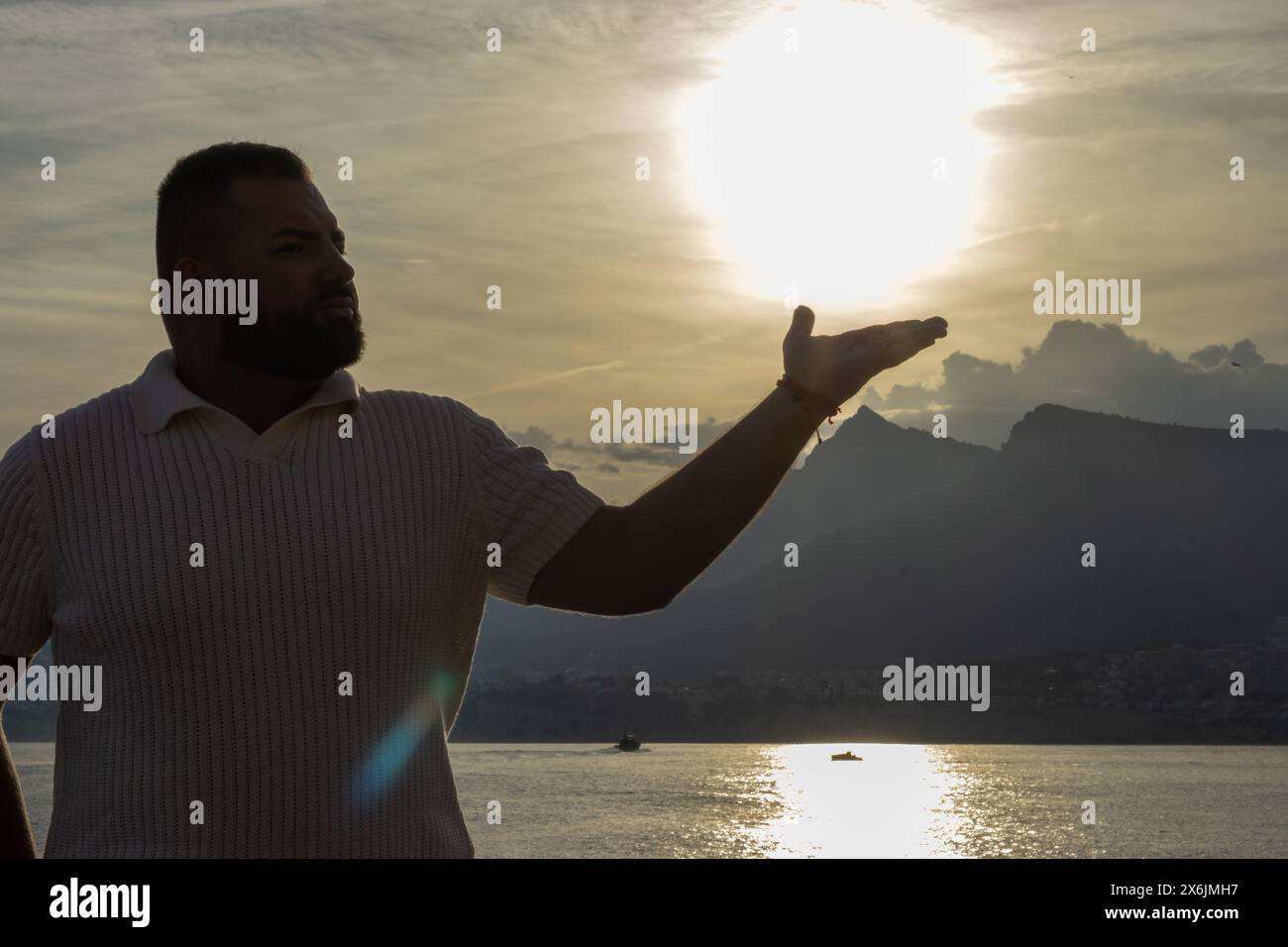 L'immagine cattura un momento toccante mentre un uomo di 30 anni si staglia di fronte a un tramonto mozzafiato. Il lago tranquillo e le montagne lontane sono Foto Stock