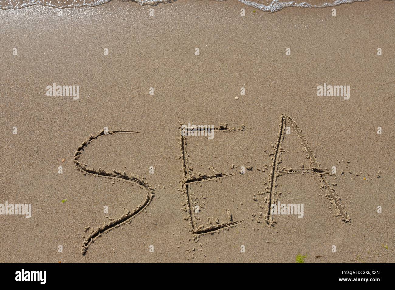 L'iscrizione mare sulla sabbia in riva al mare e l'onda crescente, spiaggia vacanza al mare. Foto Stock