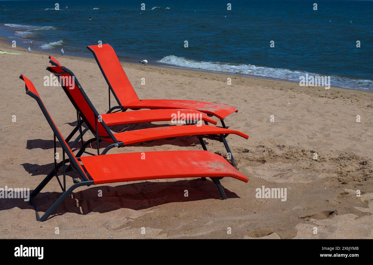 Lettini rossi sulla spiaggia. Nessuno sulle sedie a sdraio. sedia a sdraio rossa su una spiaggia di sabbia poco profonda, attrezzatura da spiaggia. Foto Stock