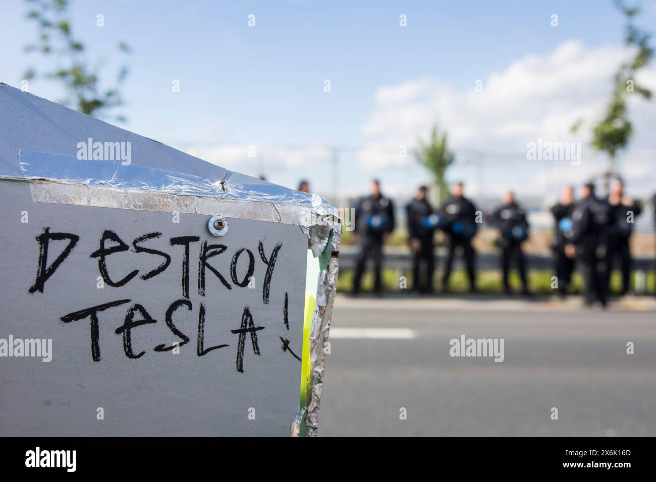 Distruggi Tesla! Slogan su un modello di Cybertruck in cartone davanti ai locali della fabbrica sorvegliato dagli agenti di polizia presso The Water. Foresta. Giustizia Foto Stock