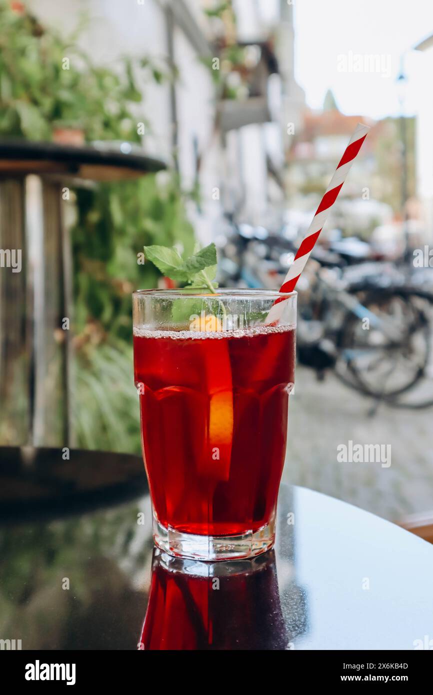 Un bicchiere di bevanda rossa (tè freddo alla frutta) con una paglia, sulla terrazza di un caffè in città Foto Stock