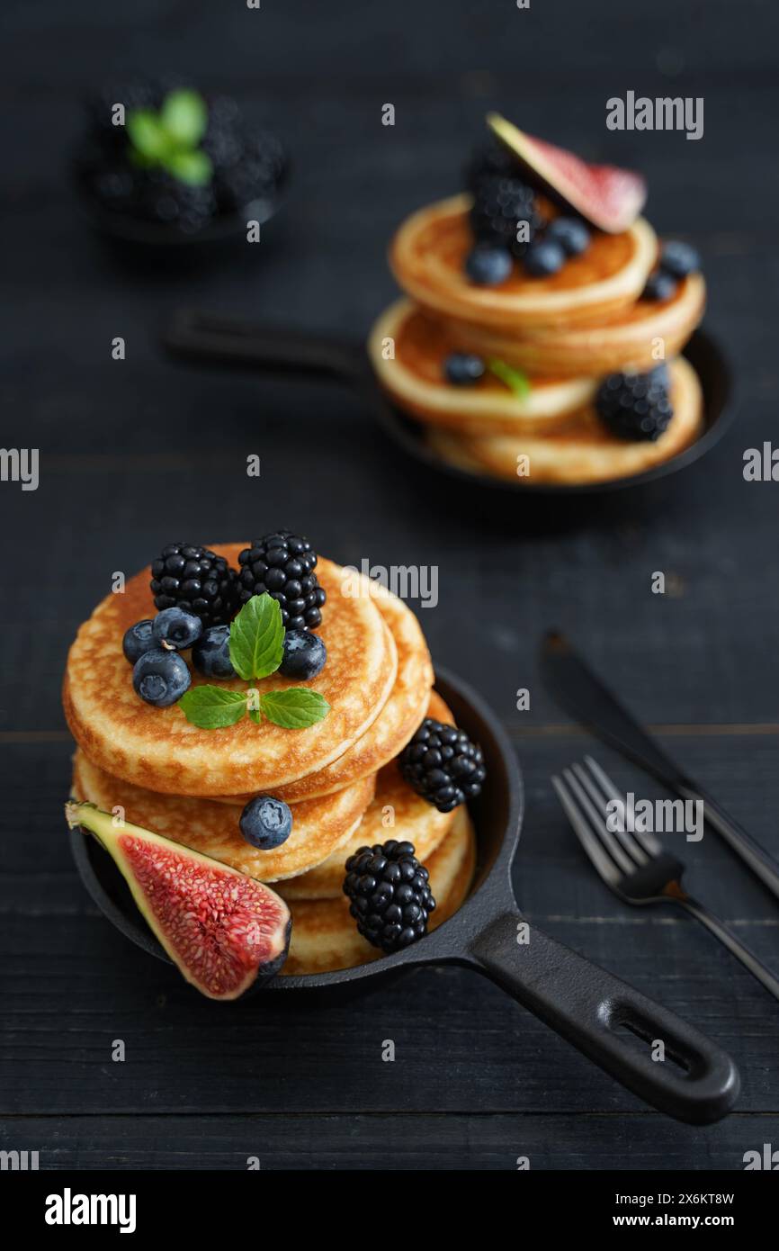 Pancake dorati su un elegante sfondo di legno nero adornato da succose bacche che trasudano calore e indulgenza Foto Stock