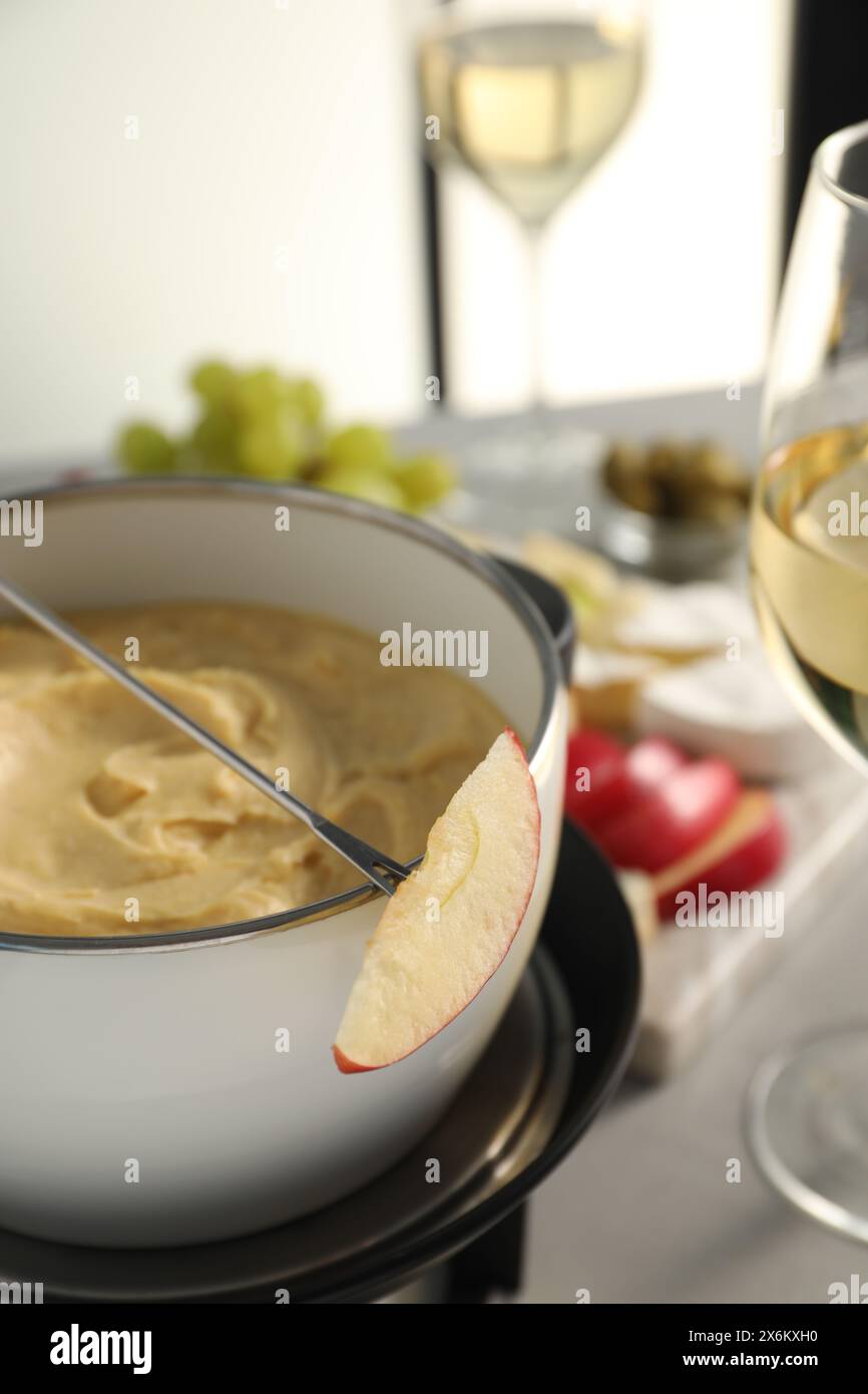 Forchetta con un pezzo di mela e formaggio fuso in fonduta su un tavolo grigio, primo piano Foto Stock