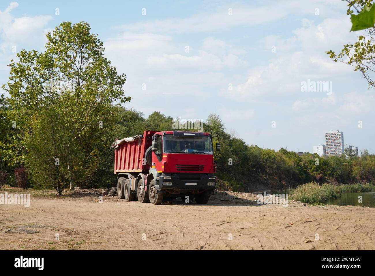 Camion ribaltabile in cantiere, su strada sterrata vicino a alberi e lago, nel quartiere Pantelimon all'interno di Bucarest Foto Stock