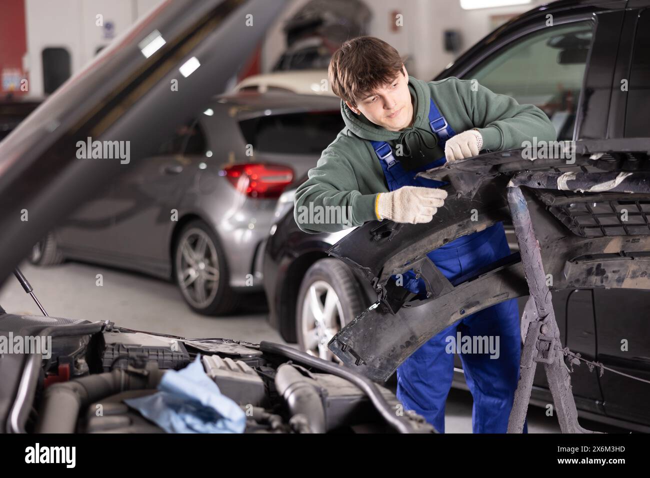 Giovane meccanico specializzato che ripara il paraurti rimosso in officina Foto Stock