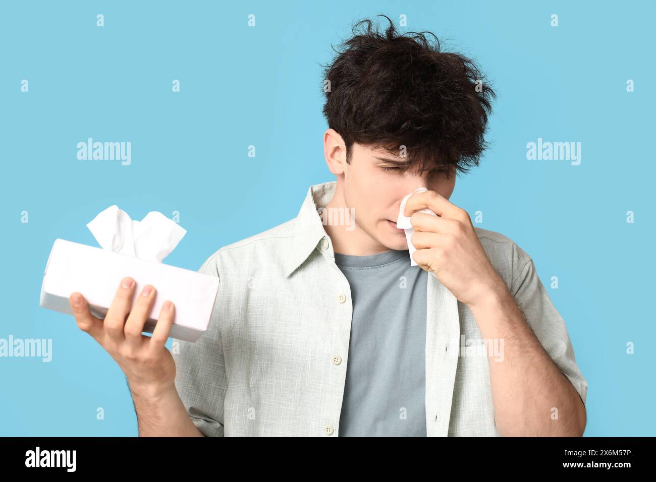 Giovane con il naso che cola su sfondo blu. Concetto di allergia Foto Stock
