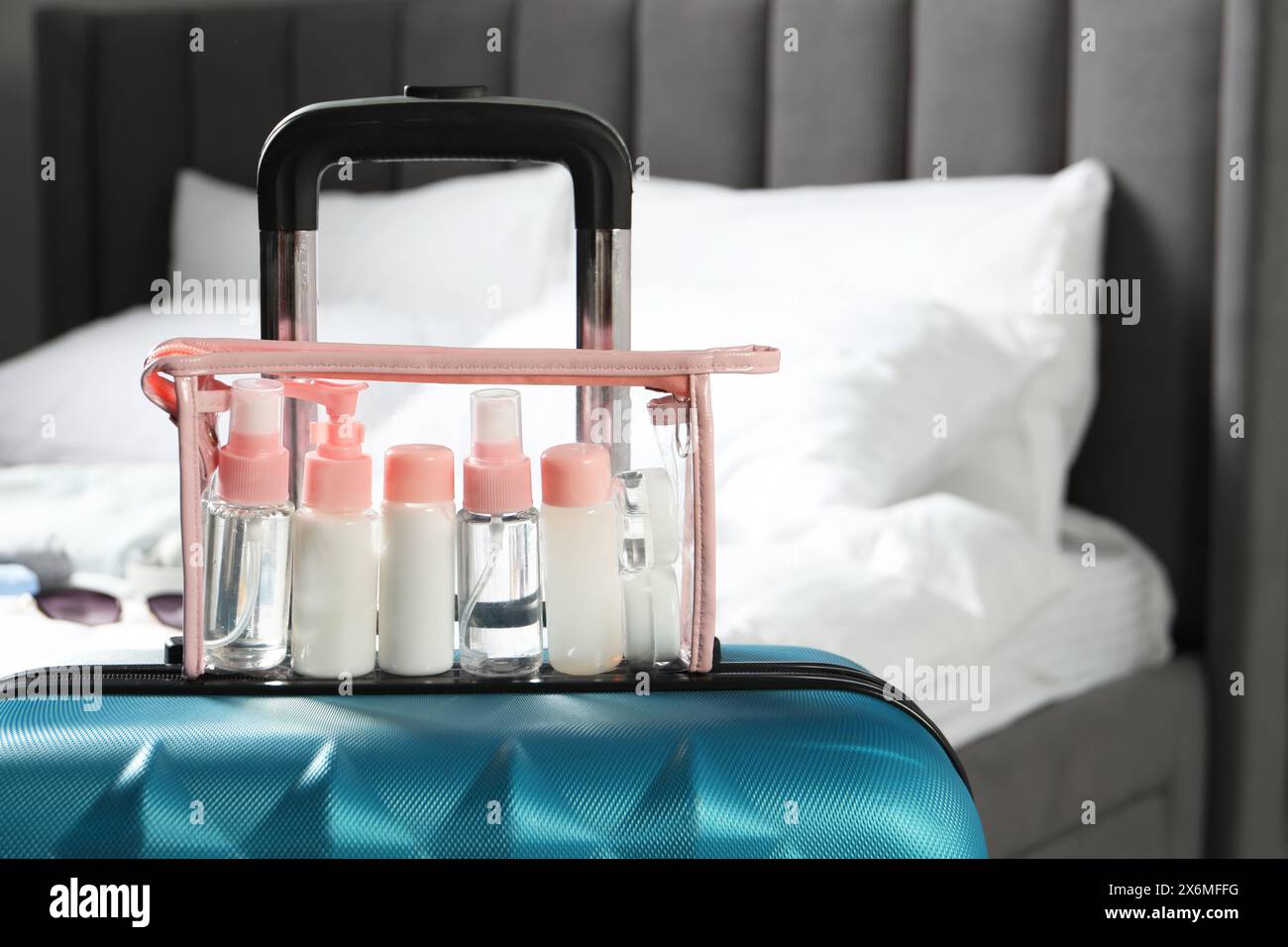 Kit da viaggio cosmetico. Sacchetto di plastica con piccoli contenitori di prodotti per la cura personale su valigia in camera da letto, spazio per testo Foto Stock