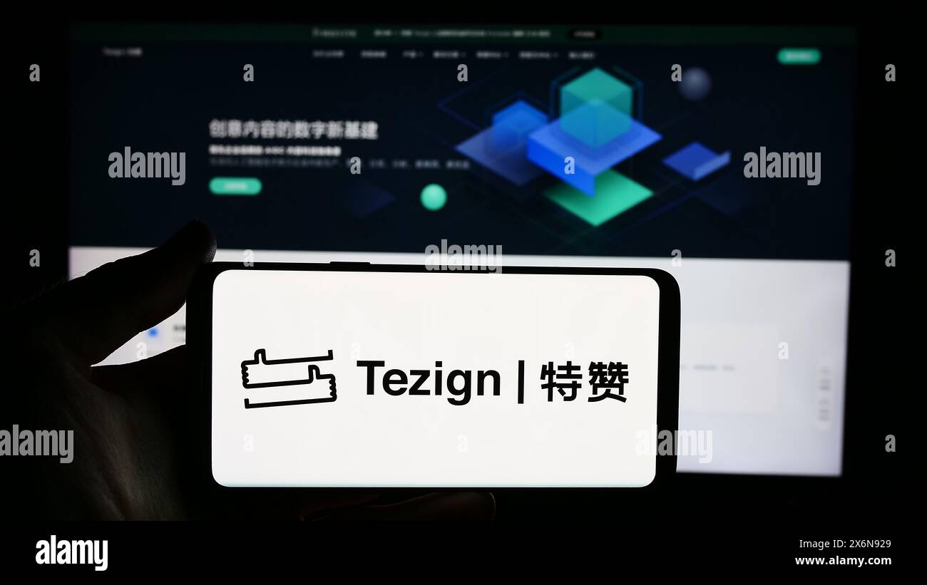 Persona che detiene un cellulare con il logo della società cinese di analisi dei contenuti Tezign di fronte alla pagina Web aziendale. Mettere a fuoco il display del telefono. Foto Stock