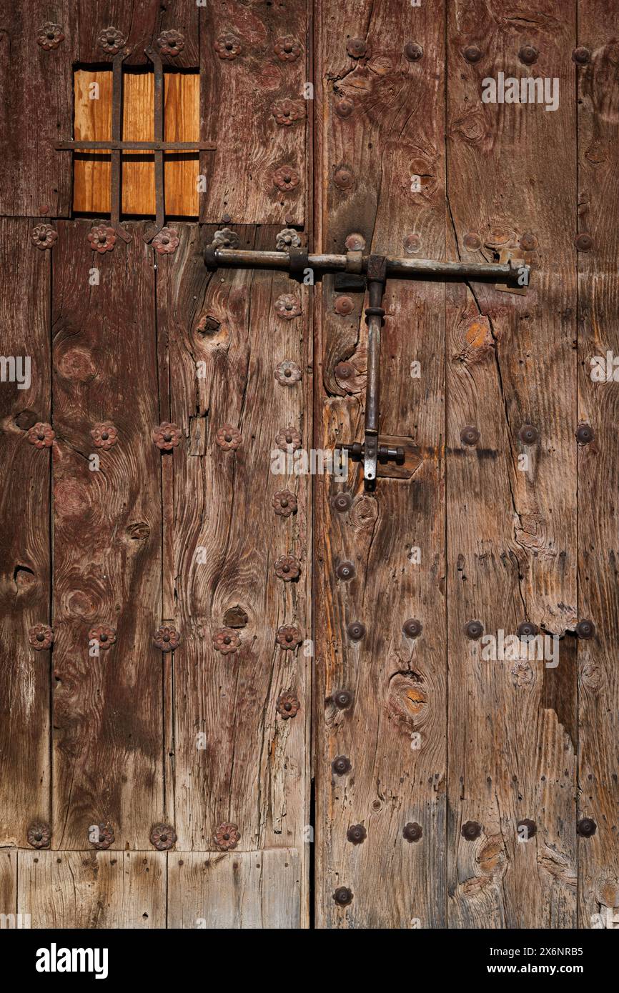 Dettaglio di una vecchia porta in legno ruvido, resistente agli agenti atmosferici, con piccola finestra e serratura a bullone in metallo. Foto Stock