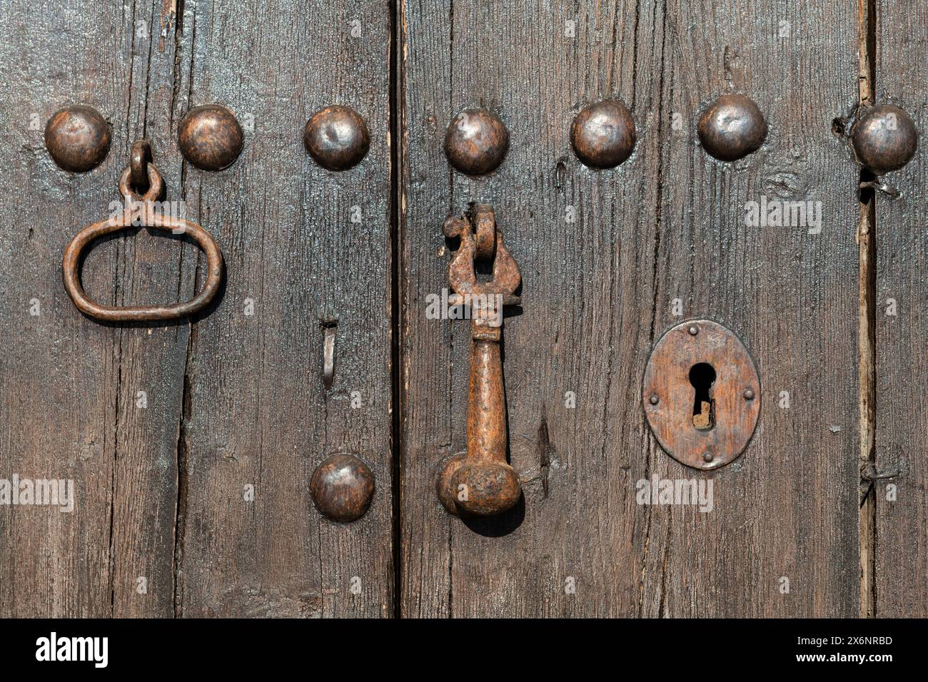 Dettaglio di una vecchia porta in legno ruvido, con rivetti metallici, buco a chiave e battitoio. Foto Stock