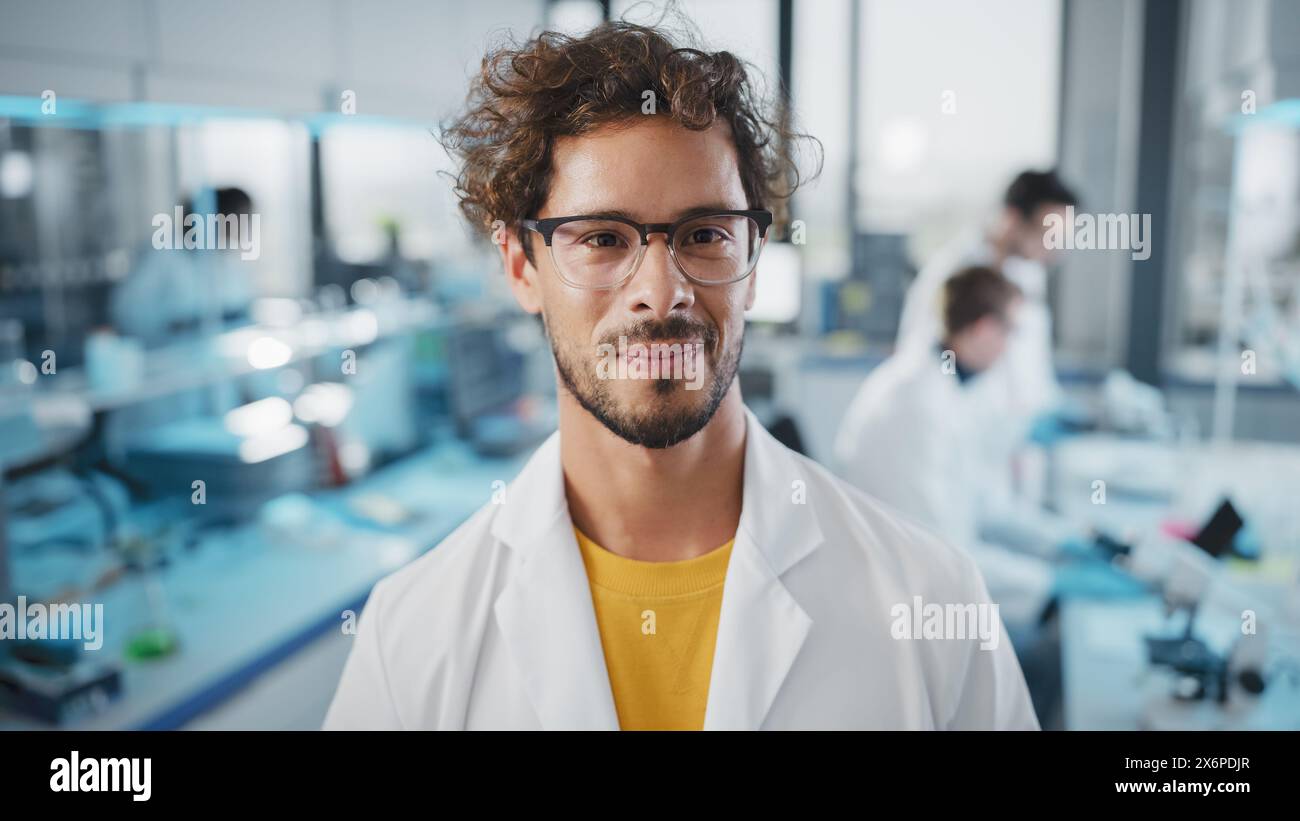 Laboratorio di scienze mediche: Ritratto di un bel giovane scienziato latino che indossa il cappotto bianco sorride guardando la fotocamera. Giovane specialista ricerca biotecnologica. Scatto verticale di primo piano medio Foto Stock