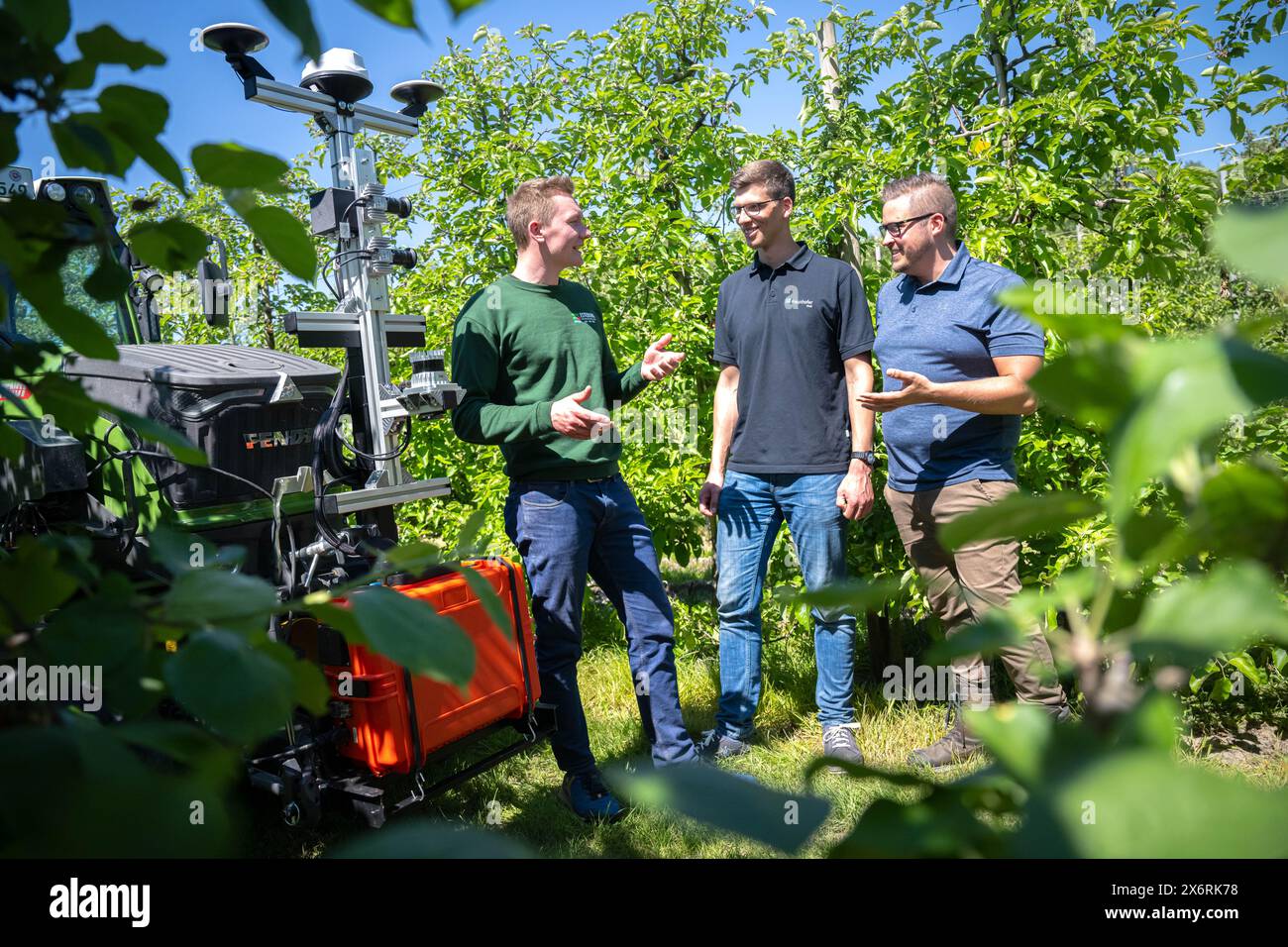 Jork, Germania. 14 maggio 2024. David Berschauer (M), Moritz Hentzchel (l) e Benjamin Schulze (r), project manager dell'Istituto Fraunhofer, si trovano accanto al trattore con la tecnologia del progetto "SAMSON" ("Smart Automation Systems and Services for Fruit Growing on the Lower Elbe") tra i meli del campo di prova di Esteburg. Con l'aiuto dell'intelligenza artificiale, un progetto di ricerca nella regione dell'Altes Land vicino ad Amburgo mira a rendere più efficiente la coltivazione della frutta. L'obiettivo è identificare meglio i parassiti e utilizzare meno sostanze chimiche. Credito: Sina Schuldt/dpa/Alamy Live News Foto Stock