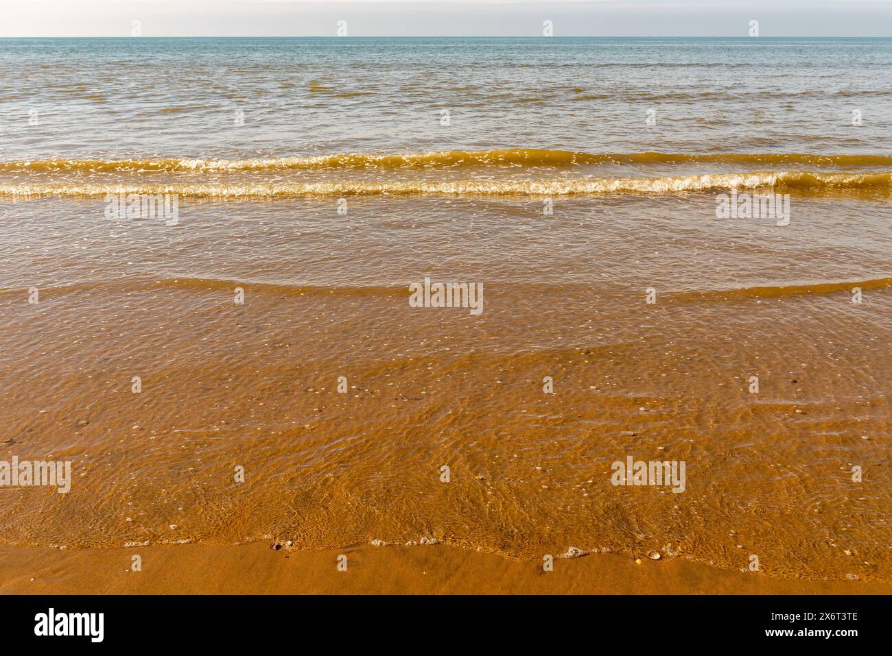 le limpide onde del mare che si innalzano coprono la sabbia dorata e l'alba Foto Stock