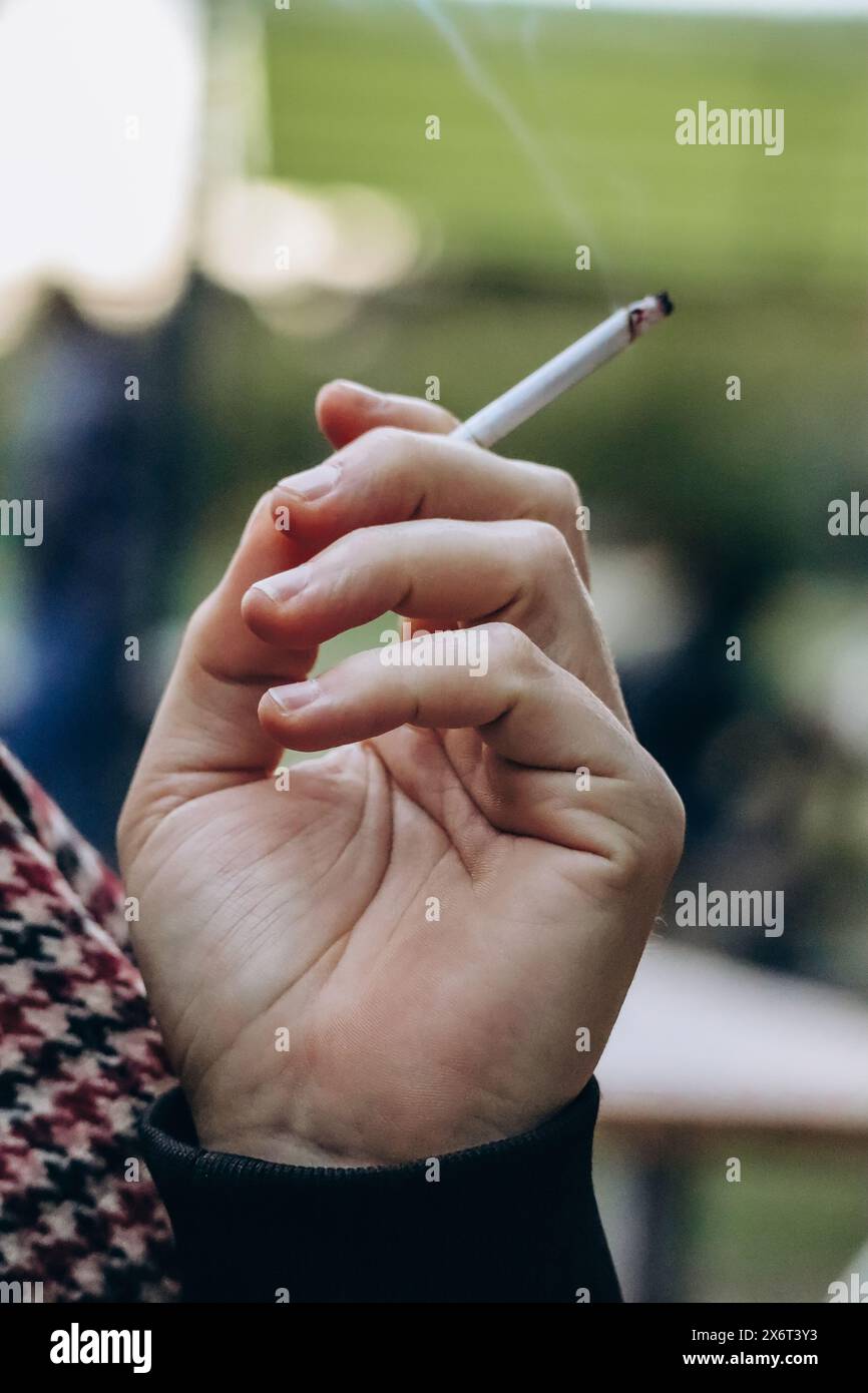 La mano di un uomo tiene una sigaretta che fuma Foto Stock