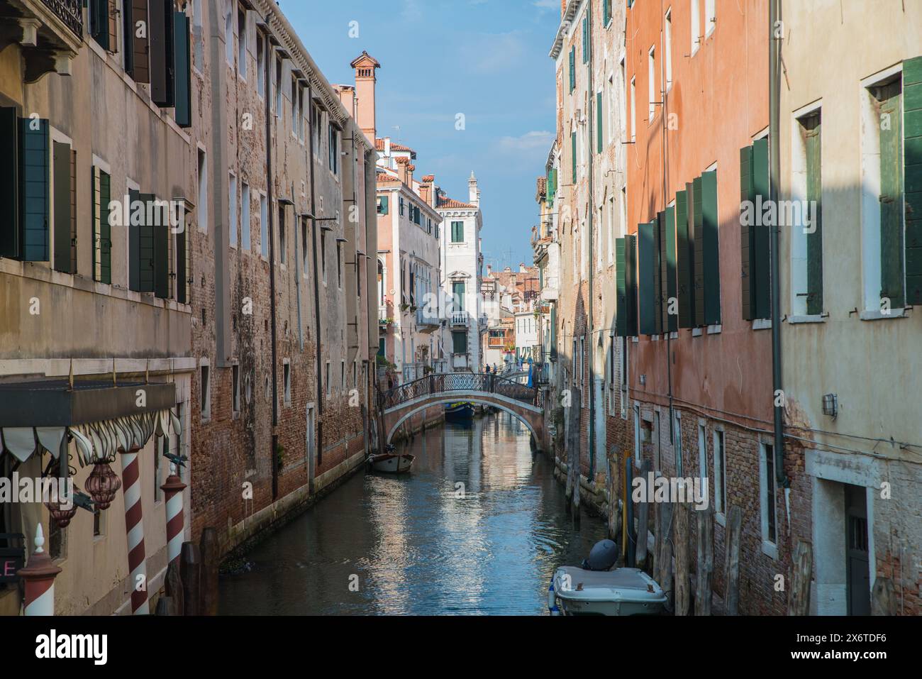 Uno dei tanti piccoli e graziosi ponti pedonali su un canale di Venezia, in Italia, ombreggiato da alti edifici su entrambi i lati Foto Stock