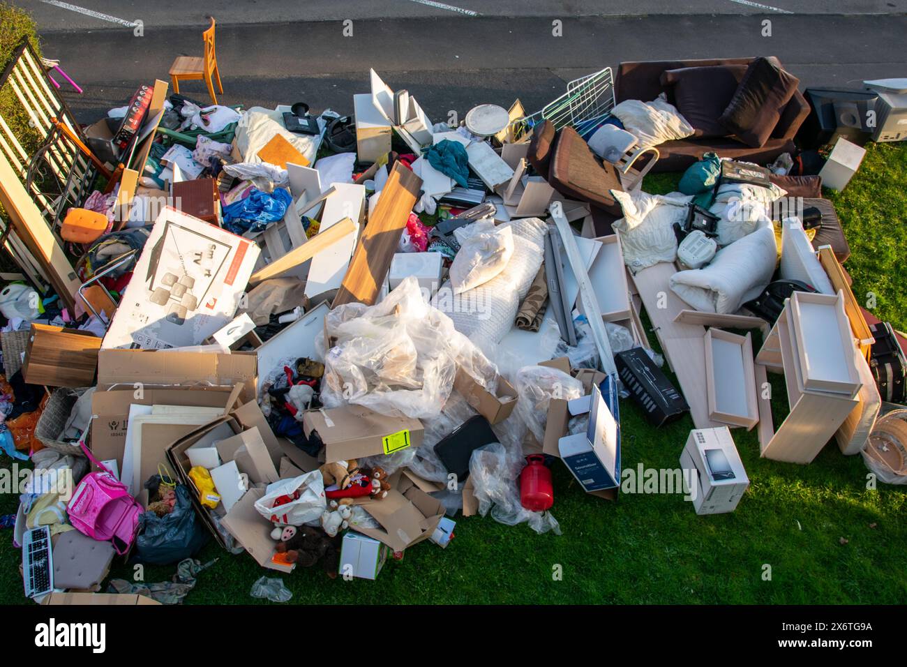 Un sacco di sprechi in una città vicino alla casa. Grande spazzatura con vecchi mobili in legno, giocattoli, scatole, sacchetti di plastica su una strada e erba verde in primavera soleggiata tra Foto Stock